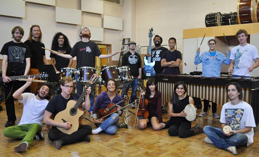 Photo of the SF State Percussion Ensemble posing with drums, guitars and a violin